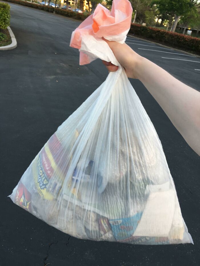 A hand holds a full bag of trash, representing the problem of trash taking over the world.