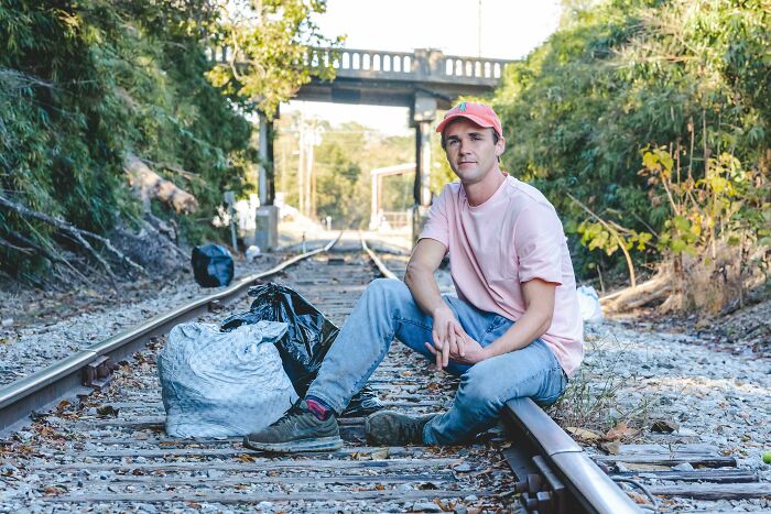 A man sits on train tracks with bags of trash beside him, highlighting the issue of trash taking over the world.