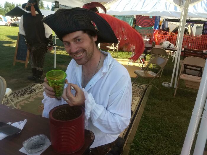 A man dressed in a pirate costume smiling while holding a cup, unrelated to the topic of trash.