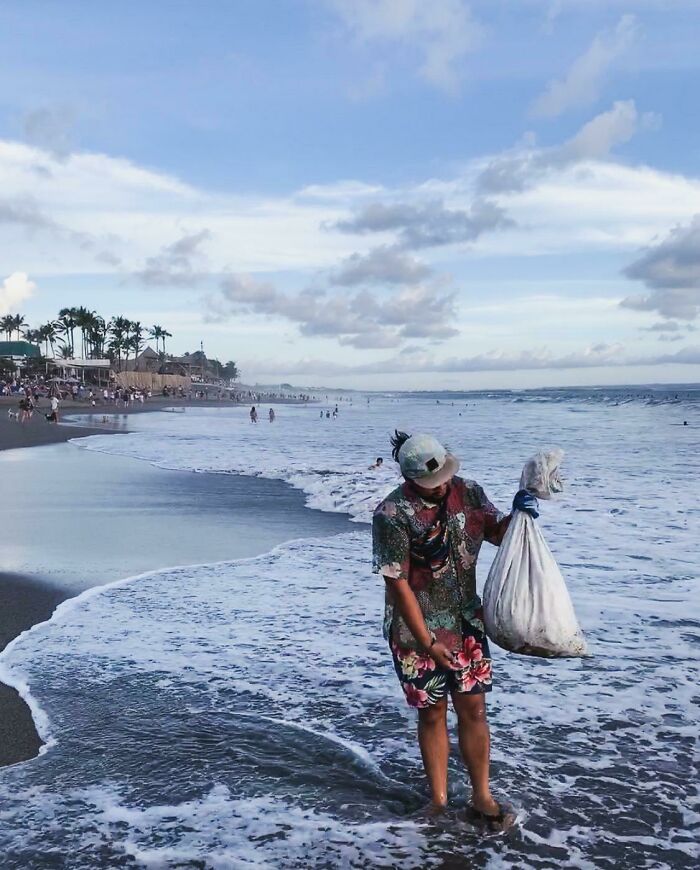 Man on a beach holding a bag full of trash as trash takes over the world.