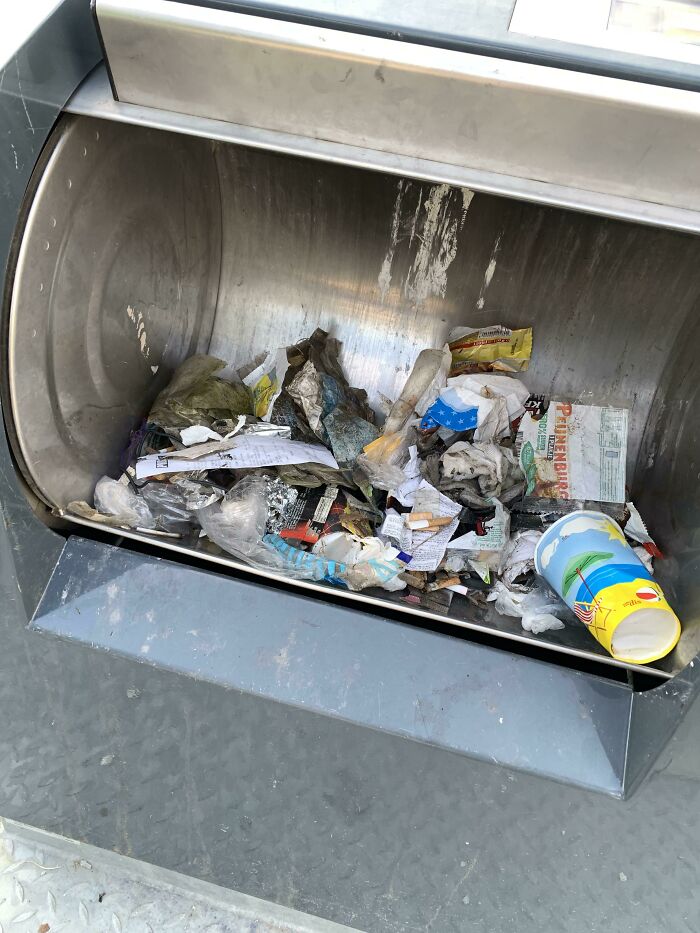 A public trash bin overflowing with various types of trash, symbolizing trash taking over the world.