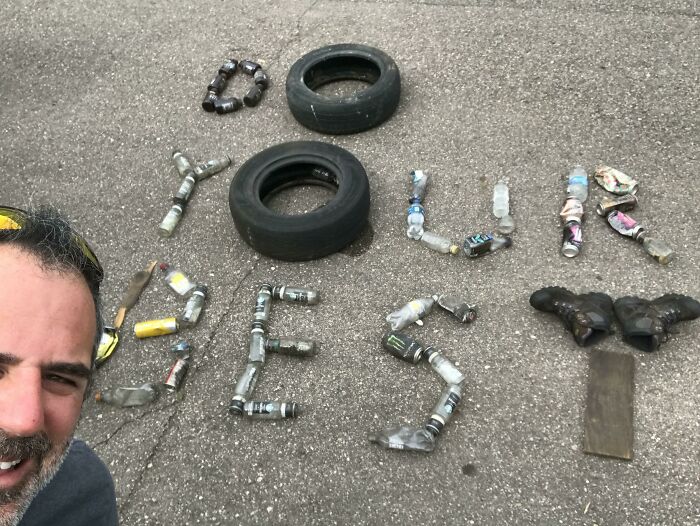 A man poses with trash arranged to spell out 'DO YOUR BEST', showcasing efforts against trash taking over the world.