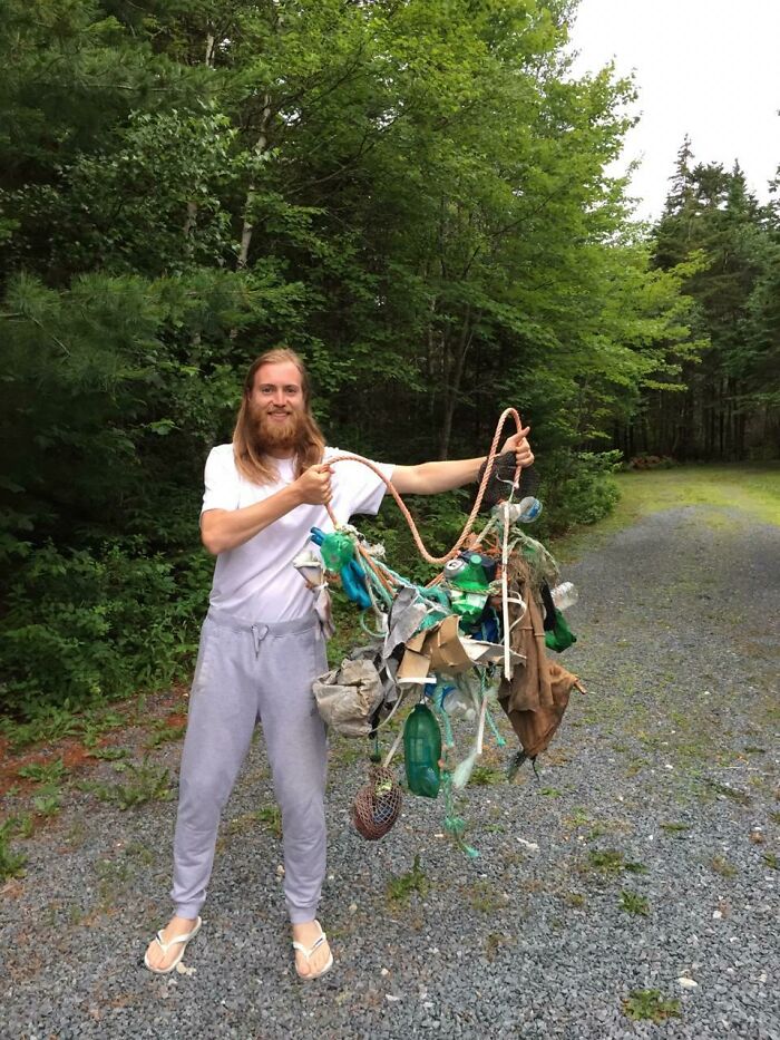 A man proudly holds a large bundle of trash he collected, highlighting the problem of trash taking over the world.