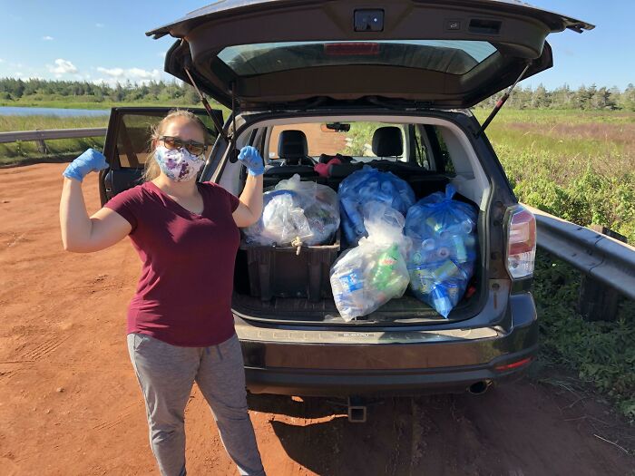 A woman wearing gloves poses beside a car filled with bags of collected trash, demonstrating efforts against trash taking over the world.