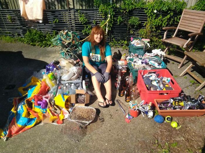 A smiling woman sits surrounded by collected trash, showing the impact of trash taking over the world.