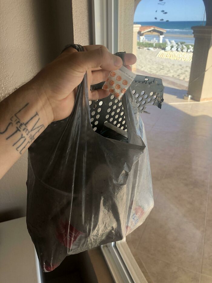 A hand holds a bag of collected trash near a beach, highlighting how trash takes over the world.