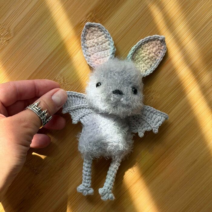Small gray crochet bat plush toy held by hand on wooden surface