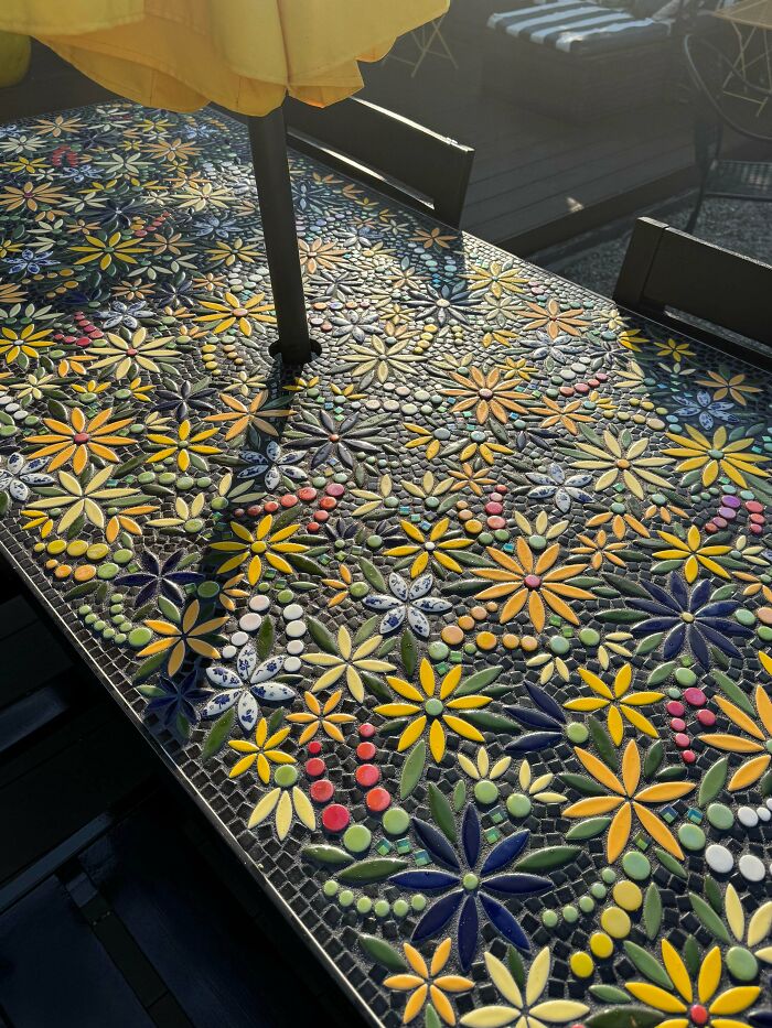 A stunning DIY home project, a mosaic table with intricate flower patterns in various colors, creating a beautiful outdoor space.