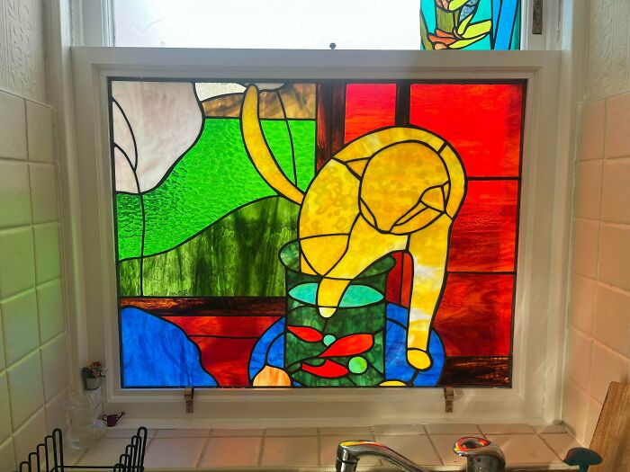 A colorful DIY home project: a stained-glass window depicting a yellow cat reaching into a fishbowl above a kitchen sink.