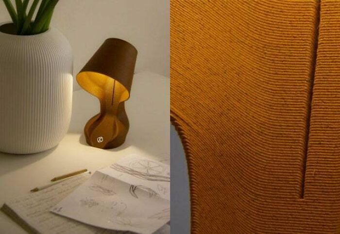 An artistic brown table lamp with a curved base, created using 3D printers, on a desk with papers.