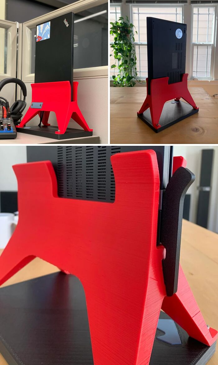 A red 3D printed vertical laptop stand holding a black laptop on a desk, demonstrating brilliant 3D printers.