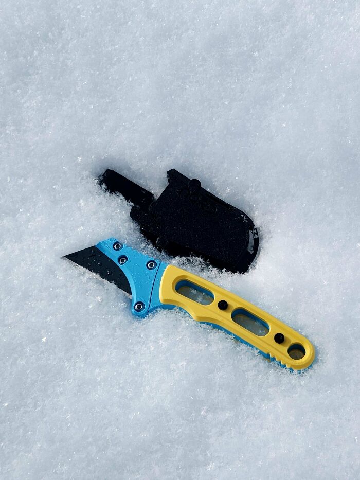 A blue and yellow utility knife and its black sheath on a bed of snow, showcasing brilliant 3D printers.