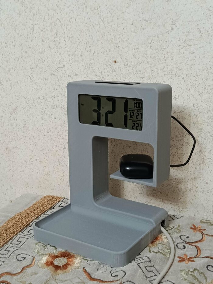 A gray 3D printed digital clock with a charging spot for earbuds, a brilliant thing made with 3D printers.