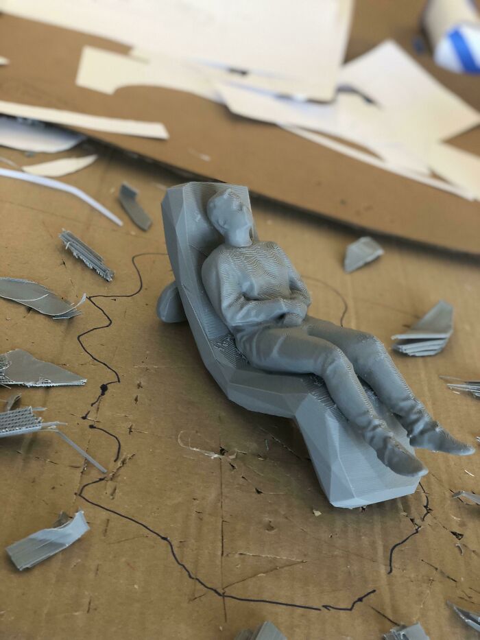 A small, gray 3D printer figure of a person reclining on a chair, surrounded by paper scraps, highlights brilliant things made with 3D printers.