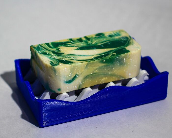 A handmade soap bar rests on a blue 3D printer soap dish, demonstrating brilliant things made with 3D printers.