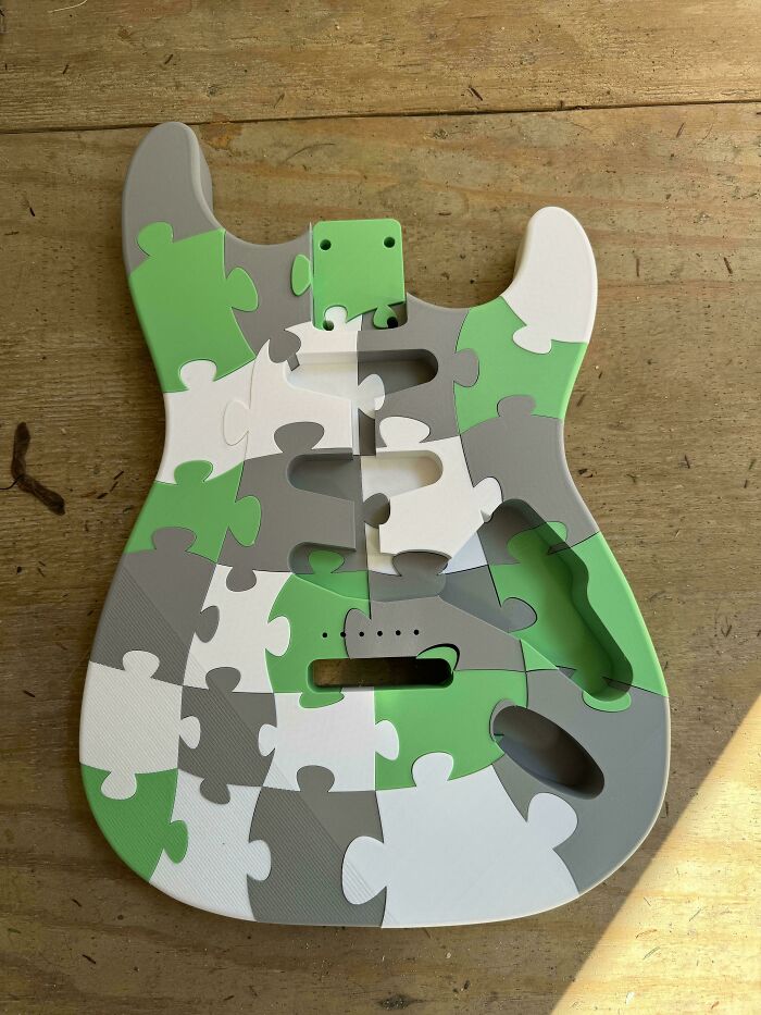 A guitar body made from interlocking green, grey, and white 3D printed puzzle pieces, demonstrating brilliant things people make with 3D printers.