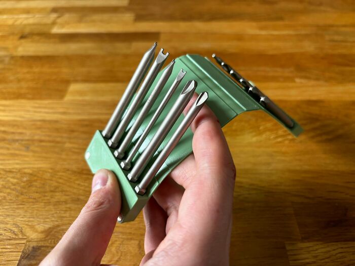 A hand holding a green 3D printed holder with various drill bits, illustrating brilliant things people make with 3D printers.