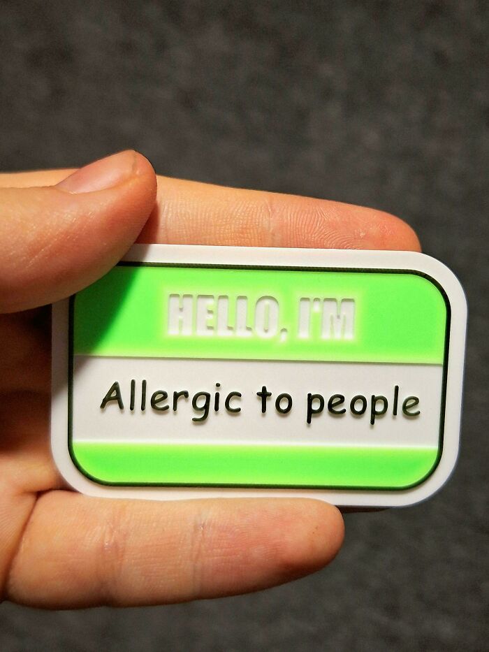 A hand holding a personalized name tag that reads Hello, I'm Allergic to people, demonstrating creative 3D printers use.