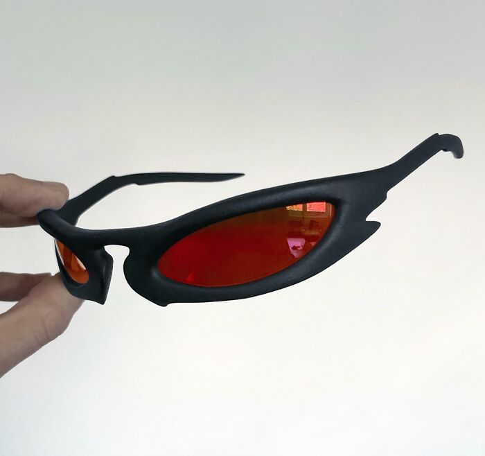 A hand holding unique black and red sunglasses, a brilliant thing created with 3D printers for custom style.