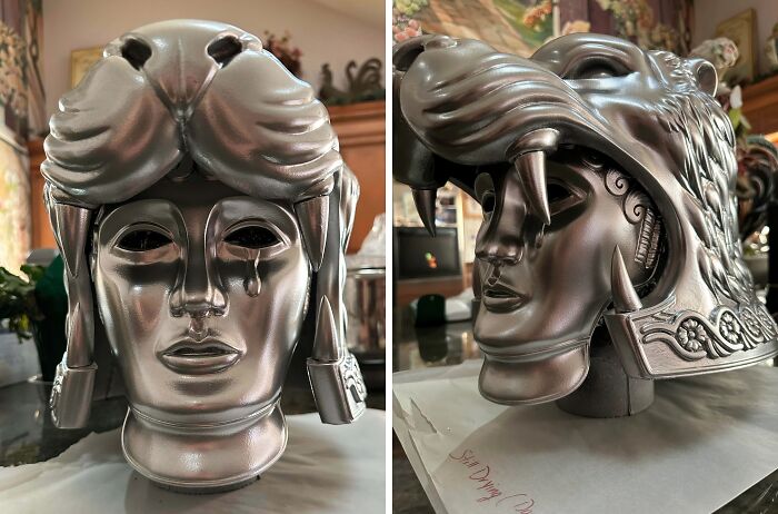 An intricately designed silver helmet with a lion's head and a weeping face, made using 3D printers.