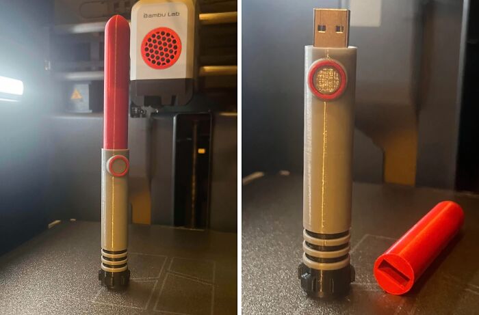 A red and grey 3D printed lightsaber handle next to a 3D printer, transforming into a USB drive, demonstrating brilliant things made with 3D printers.