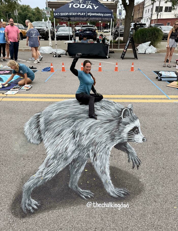 A woman sits on a 3D street art raccoon, a weird and wonderful sight.