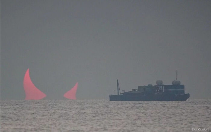 A large ship at sea with two red horn-shaped sun reflections, a weird and wonderful picture of the world.