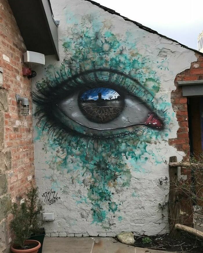 An eye painted on a brick wall with green and teal splatters, representing a weird and wonderful world.