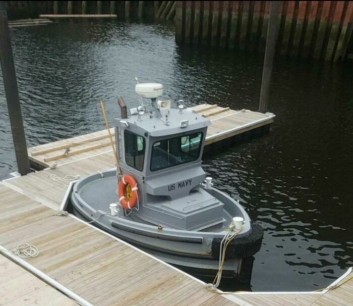 A small gray US Navy tugboat docked at a wooden pier, an example of the weird and wonderful vessels of the world.