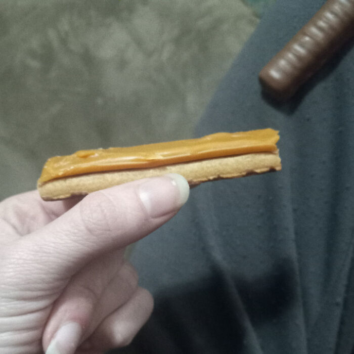 A hand holds a biscuit topped with orange caramel, a chocolate bar in the background, a weird and wonderful snack.
