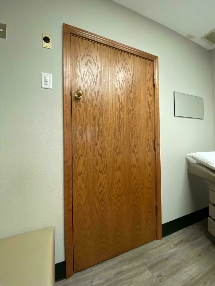 A closed wooden door with a brass doorknob in a room with light green walls and a medical examination table, part of the wonderful world.