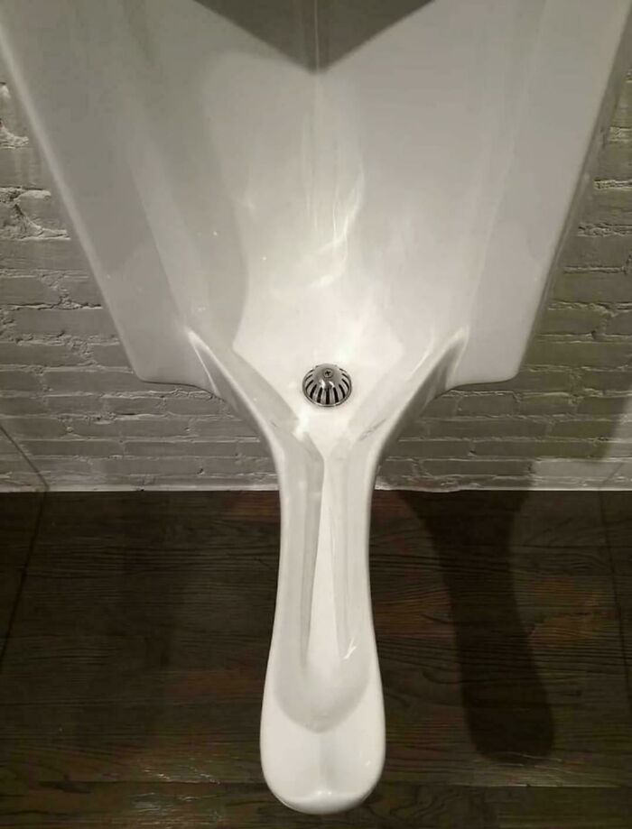 A white, elongated, modern urinal with a metal drain, illustrating the weird and wonderful aspects of design.
