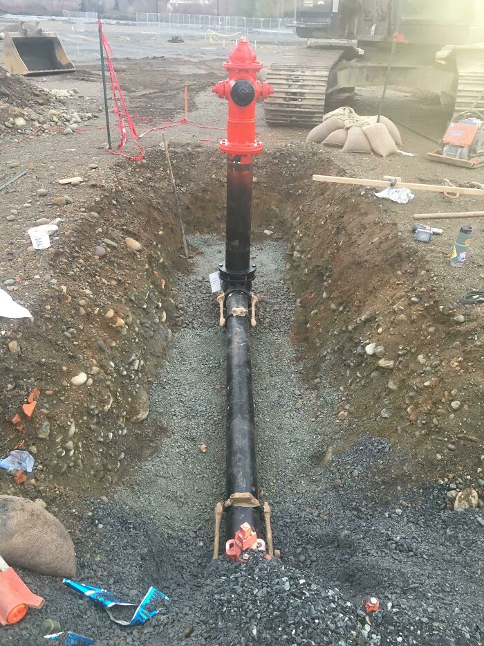 A red fire hydrant connected to a newly installed pipe in a trench, a wonderful and weird sight of construction.