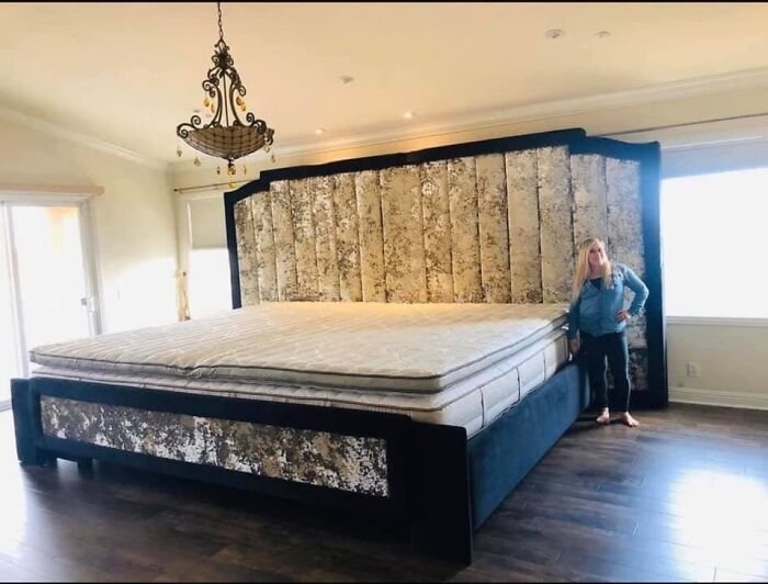 A woman standing next to an enormous bed in a spacious room, highlighting the weird and wonderful aspects of interior design.