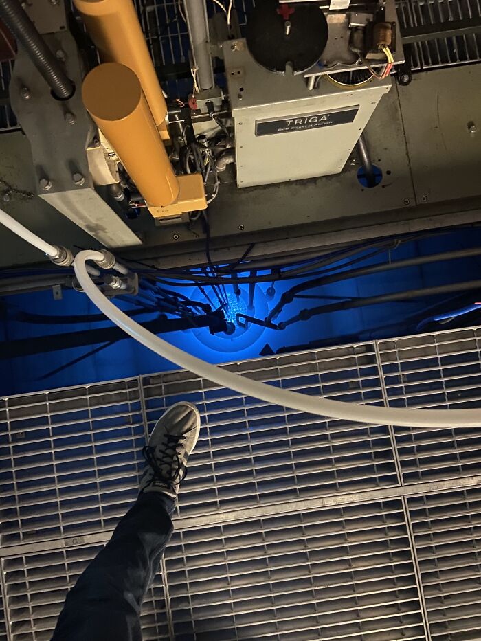 A person's foot on a metal grate looking down at a glowing blue light in an industrial setting, a wonderful world sight.
