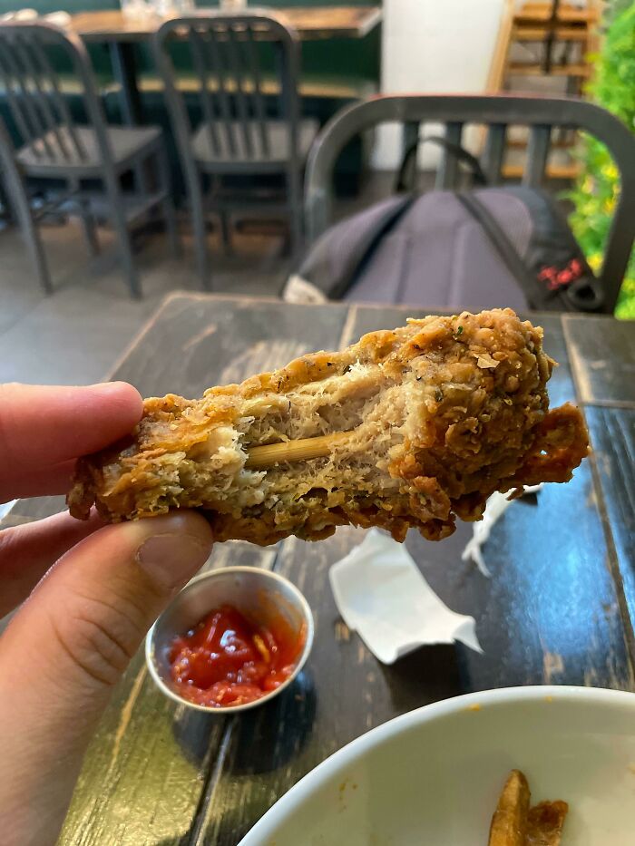 A hand holding a piece of fried chicken with a toothpick stuck through it, showcasing the weird and wonderful side of food.