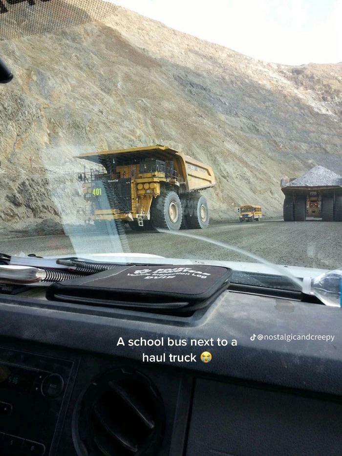 A small school bus dwarfed by giant haul trucks in a mine, a weird and wonderful sight.