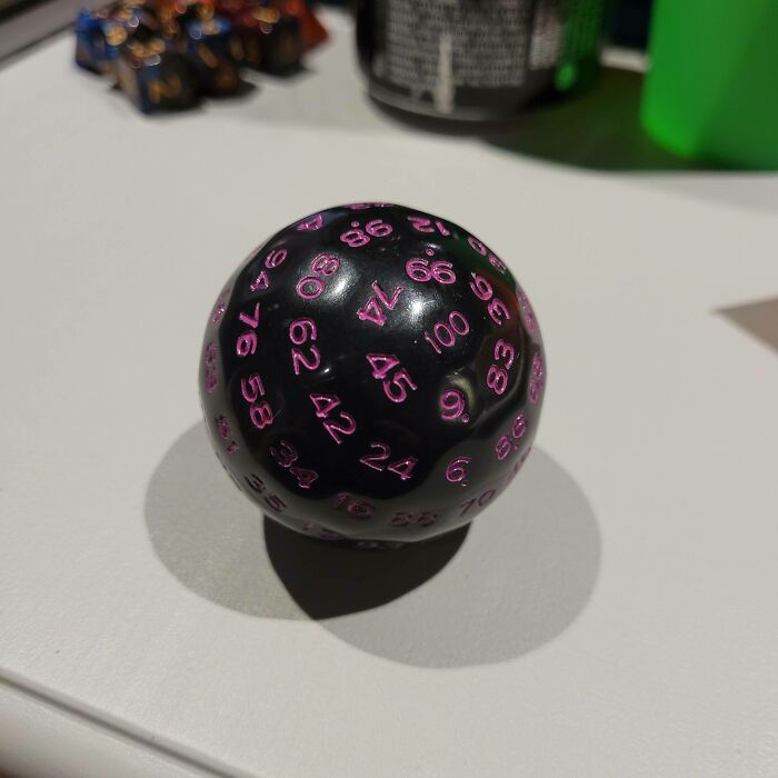 A black 100-sided d*e with pink numbers, a weird and wonderful object.