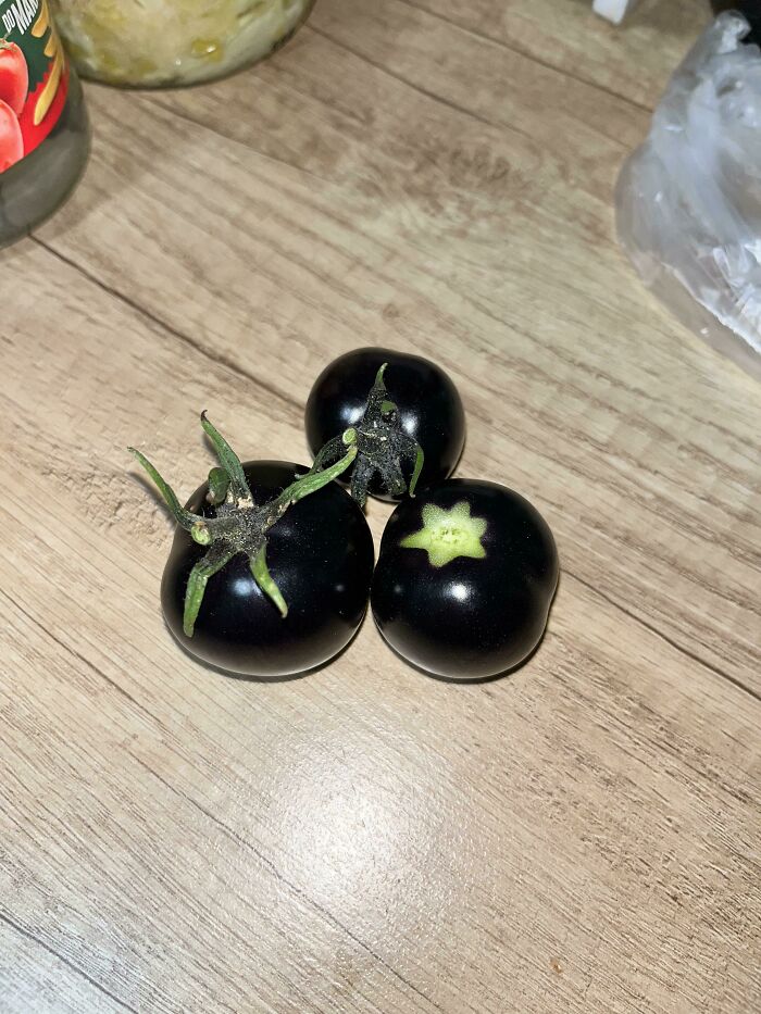 Three small, dark purple-black tomatoes on a wooden surface, showing the weird and wonderful nature of produce.
