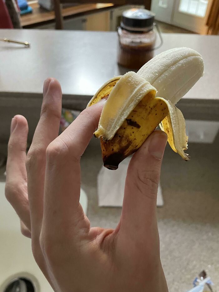 A hand holding a tiny, peeled banana, showcasing the weird and wonderful world.