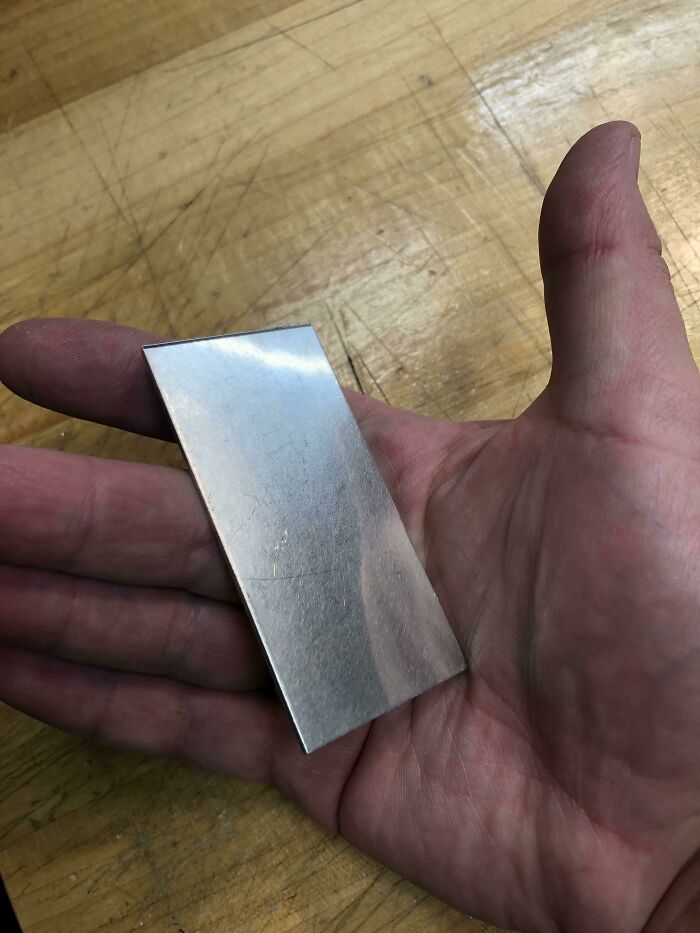 A hand holding a thin, reflective metal strip, highlighting the wonderful and weird simplicity of materials.