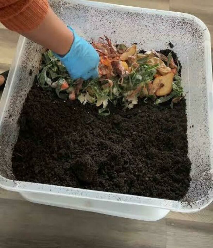 A gloved hand adds food scraps to a bin of dark soil for composting, a common side hustle.