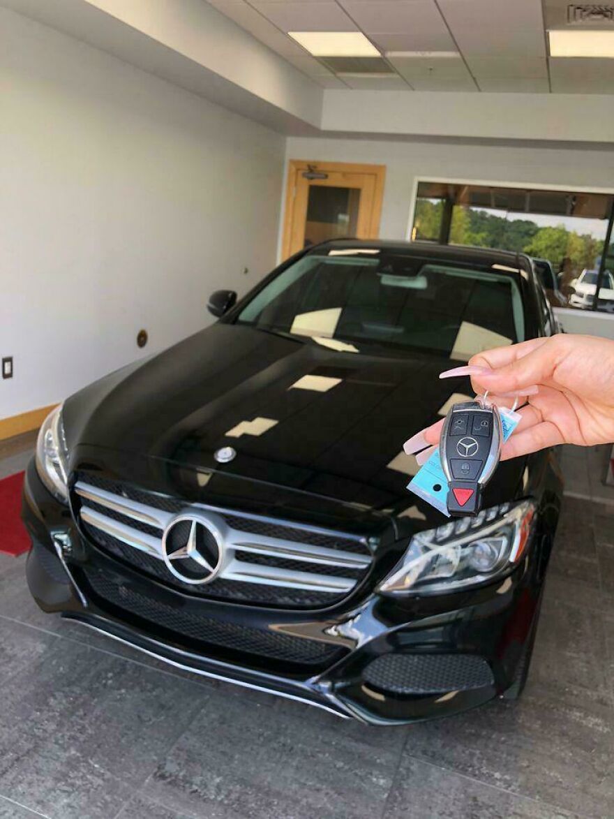 A hand holding car keys with a Mercedes logo in front of a shiny black Mercedes car, a weird side hustle.
