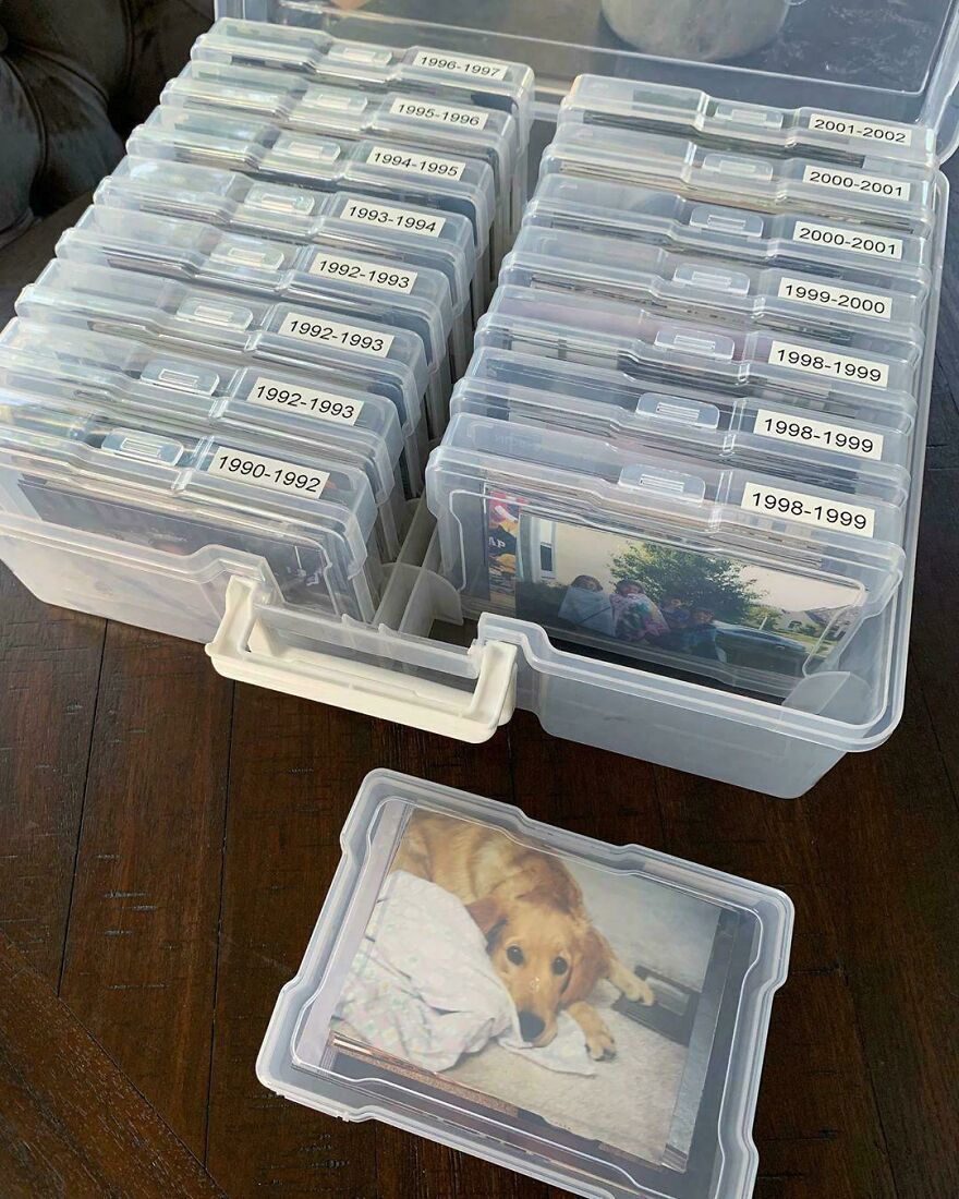 Clear plastic storage boxes with labeled photos, organized by year, showing a side hustle of photo archiving.