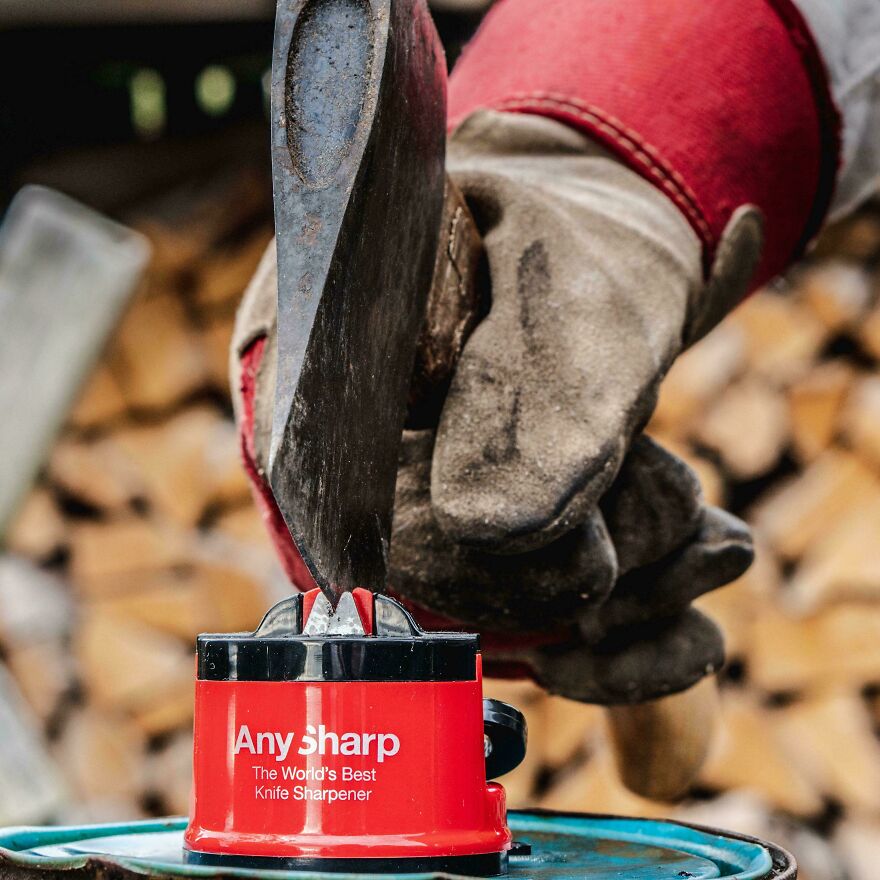 A person in work gloves sharpens an axe with a red Any Sharp sharpener, demonstrating a side hustle.