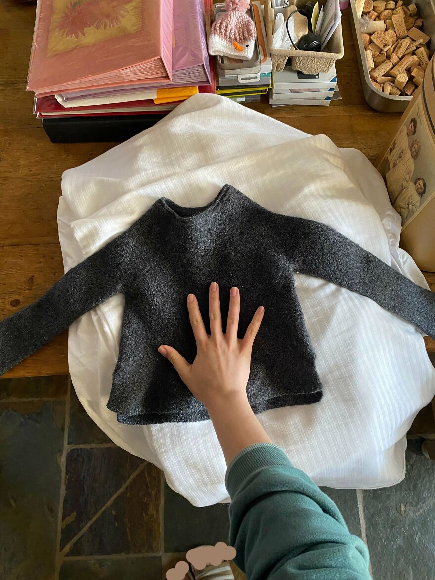 A hand on a shrunken grey sweater, a funny unfortunate regret due to a laundry fail.