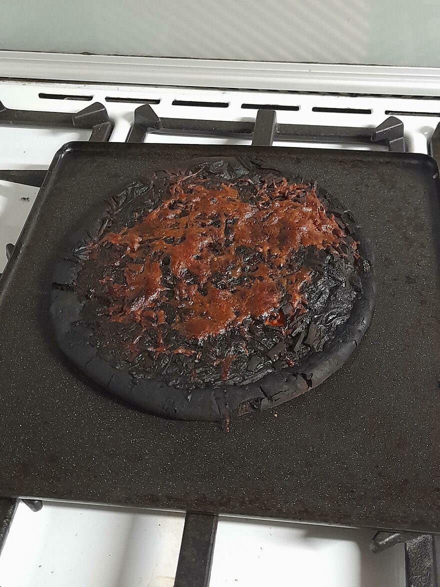 A completely burnt and unappetizing pizza on a baking sheet, a funny cooking fail.