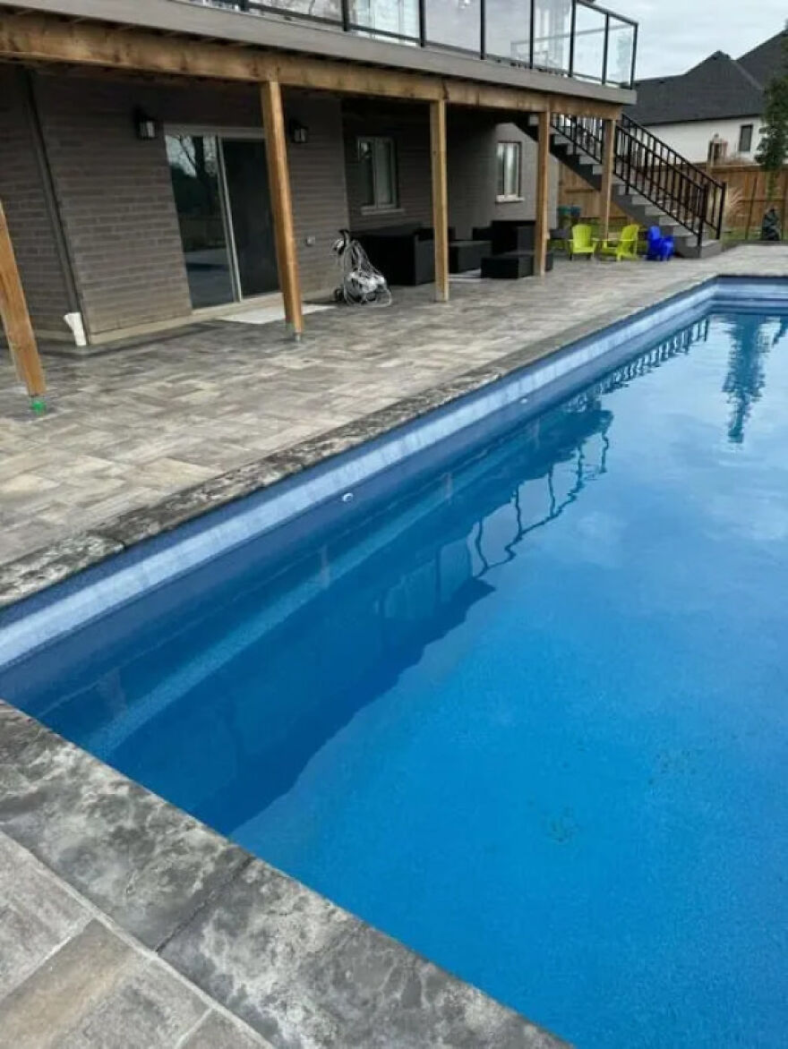 An in-ground swimming pool with stone patio and a house with a deck in the background, showing a home improvement side hustle.