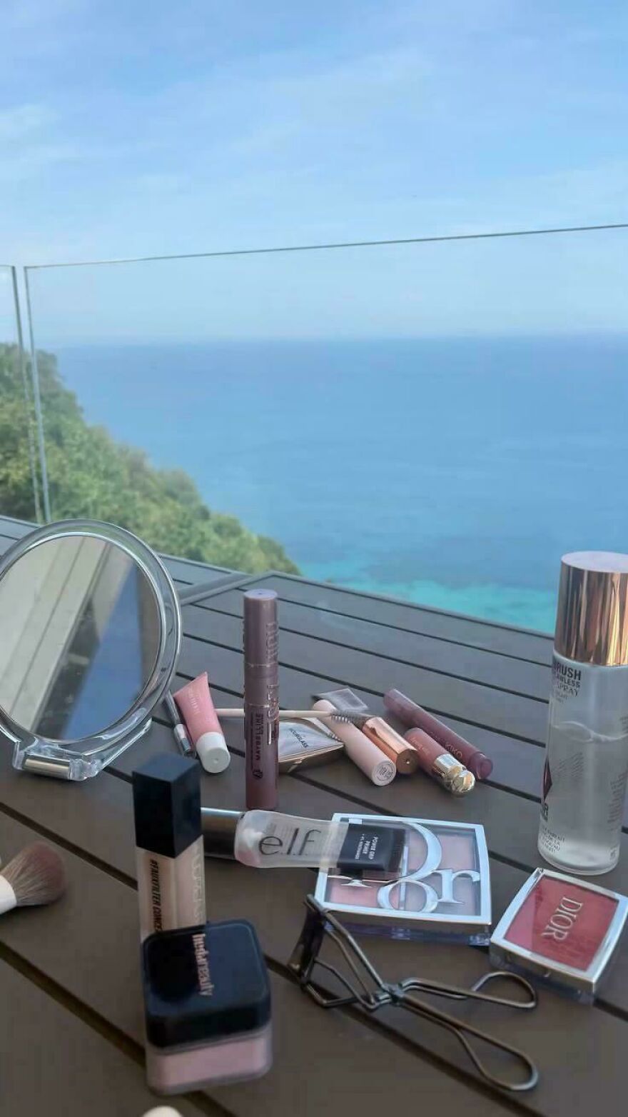 Various makeup products laid out on a table with a scenic ocean view, potentially for a beauty-related side hustle.