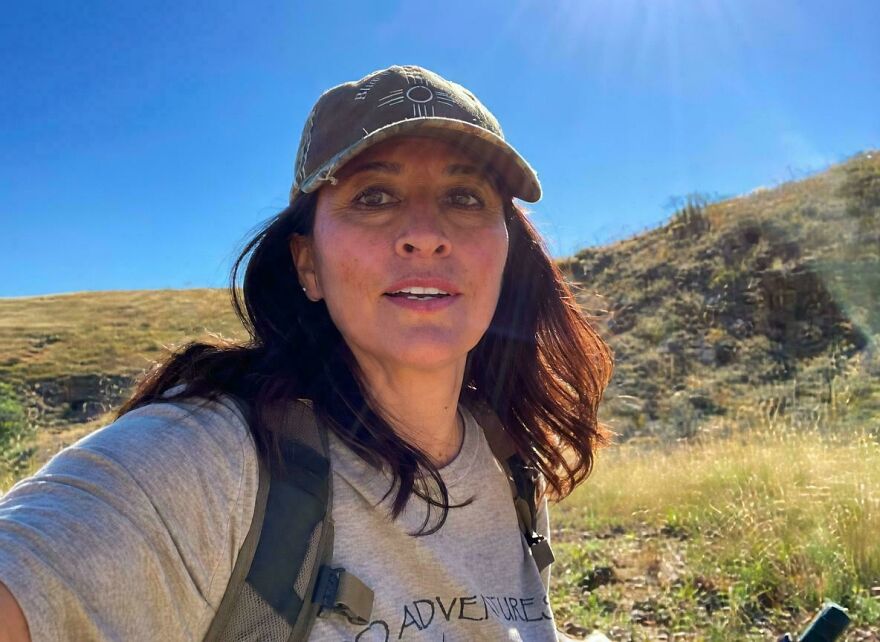 Woman in a cap and backpack, smiling, hiking outdoors on a sunny day. A strange thing happening on Earth.